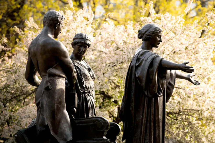 Statue of Alma Mater with Learning, and Labor in front of yellow and white spring blooming trees.