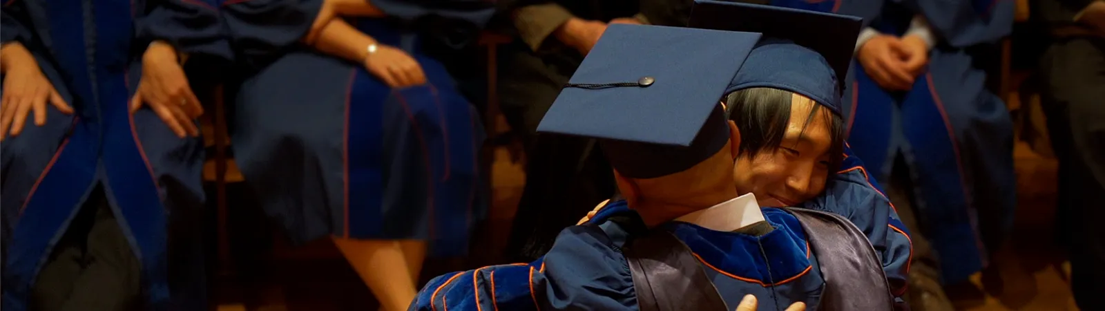 graduate and mentor hugging at doctoral hooding ceremony