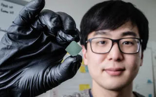 llinois mechanical science and engineering student and lead author of a new study Benjamin Sohn holds a device that uses sound waves to produce optical diodes tiny enough to fit onto a computer chip. 